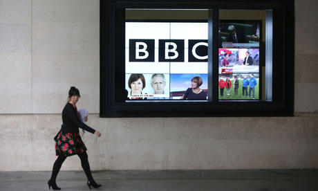 woman walks past giant screen showing BBC logo