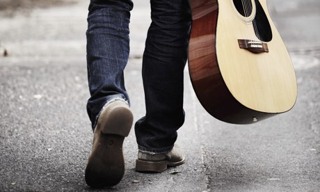 Man carrying a guitar down street.