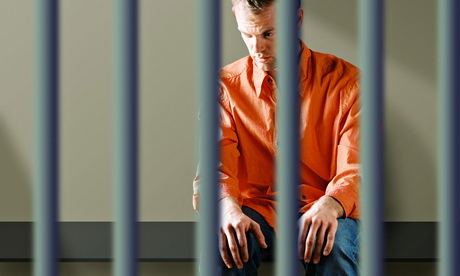 A young sits in a jail cell looking sad and depressed