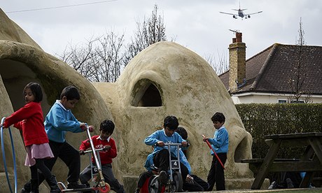 Pupils of Hounslow Heath school play around the huts in the playground as another low jet flies in