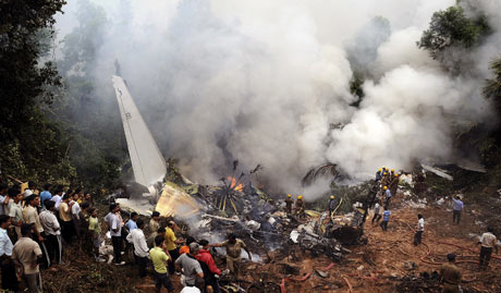 Civilians look on as Indian firefighters gather at the site of an  Air India plane crash in Mangalore