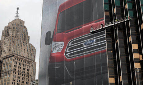 Workers hang a Ford Motor banner on the side of a building across from Cobo Center