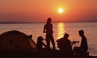 Ryhmä ihmisiä camping rannalla auringonlaskun aikaan