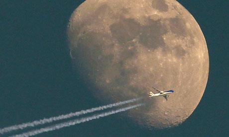 A jet it's vapour trail streaming out behind flies past the waxing moon over the city of Aarau