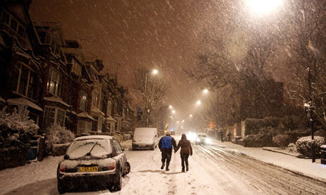 A couple walk up Muswell Hill, north London as cars struggle to drive through the snow