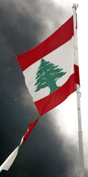 Black smoke rises behind a tattered Lebanese flag.