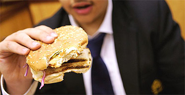 A schoolboy eats a burger for lunch