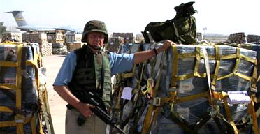 An armed guard poses beside pallets of $100 bills in Baghdad