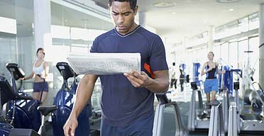 A man walking on treadmill reading the paper