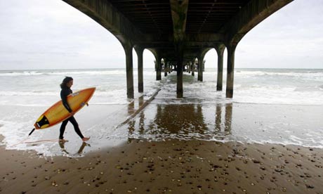 A surfer walks under Boscombe pier in Dorset