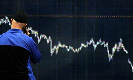 A man talks on his phone as he stands in front of a financial display board in central London today
