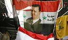 A flag carrying the face of the Syrian president, Bashar Assad, sits atop a  Lebanese flag in a market in Damascus