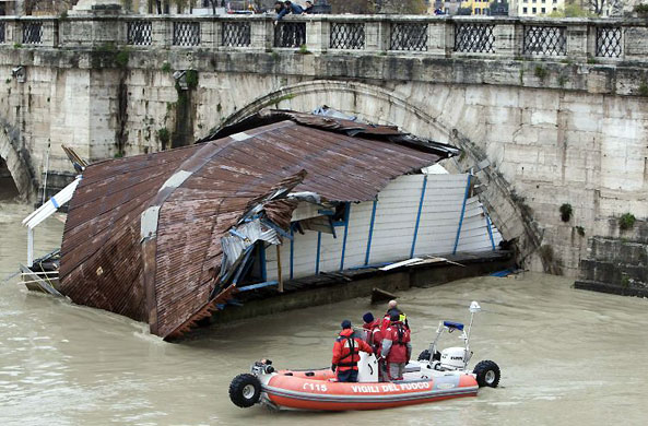 Gallery December 12 2008: Rome, Italy: Rescuers look at a boat that is caught in the arch of a bridge