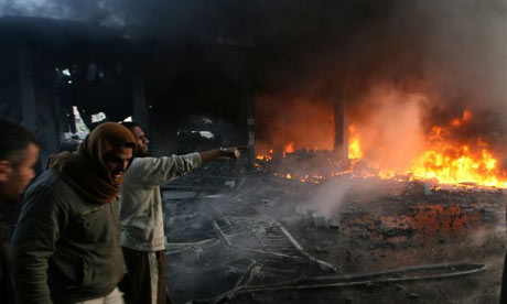 Palestinian men look on as flames rise from debris at the site of an Israeli air strike in Rafah, Gaza