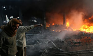 Palestinian men look on as flames rise from debris at the site of an Israeli air strike in Rafah, Gaza