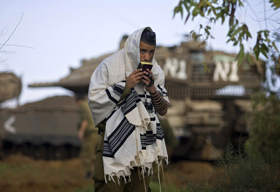 Gallery Israeli missile strikes: An Israeli soldier prays in front of a tank near Israel's border