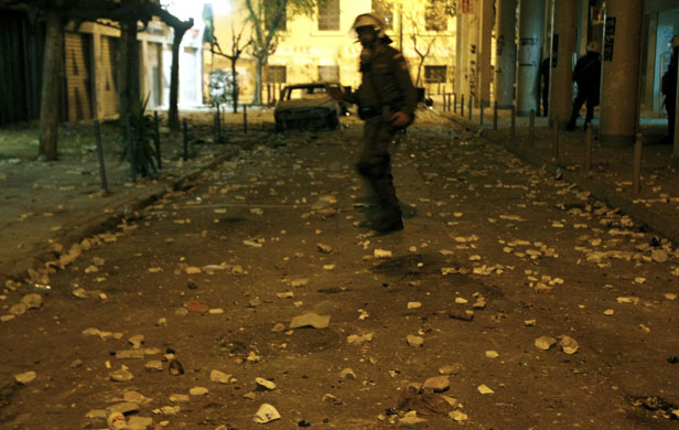 Gallery Riots in Athens: A policeman crosses a street littered with stones during riots in Athens