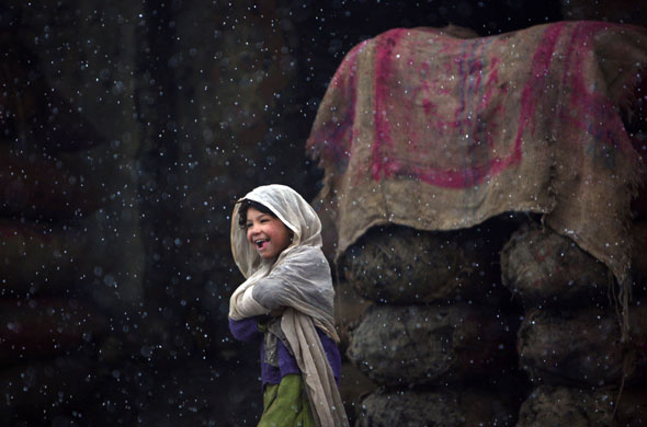 Gallery 24 hours in pictures : A girl smiles as she walks on a road as snow falls in Kabul