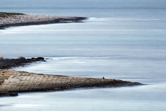 Gallery 24 hours in pictures: A fisherman sits on the rocks along the shoreline in Bahar ic-Caghaq