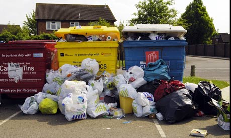 Plastic bags filled with plastic bottles litter the area in front of the local recycling point