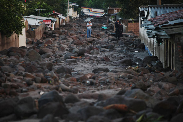 El Salvador hurricane: A man stands in a street covered with rocks from a landslide in Verapaz