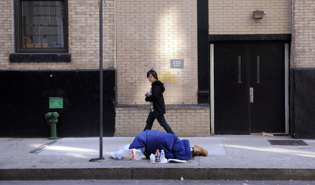 Homelessness: A woman walks past a man sleeping on a street in New York