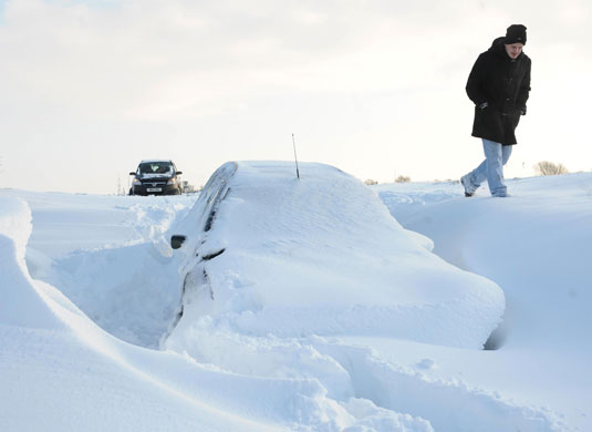 Snow in the UK: A man walks past an abandoned car buried in a snow drift near Royston