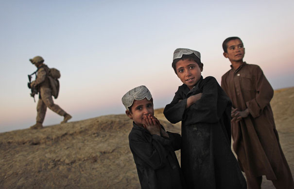 24 Hours: A US Marine walks past Afghan youths during a patrol near Khan Nashin