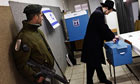 An Israeli policeman stands guard as a Jewish Orthodox man casts his vote at a school in Jerusalem
