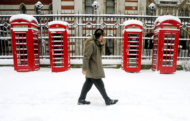 Gallery Snow in England: London: A man chats on his phone as he passes telephone boxes.