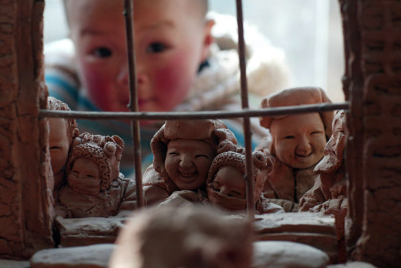 Gallery 8 February 2009: Yangjitun, China: A child looks at a set of clay figures made by a villager
