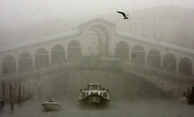 Venice in decline: A water bus passes under the Rialto bridge in the fog in Venice.