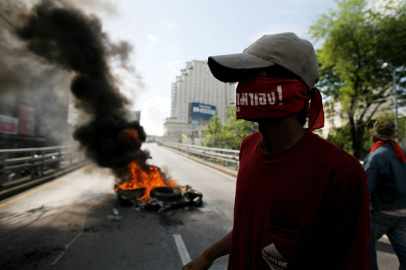 Thailand protests: A protestor walks past burning tyres at a protest near Victory Monument.
