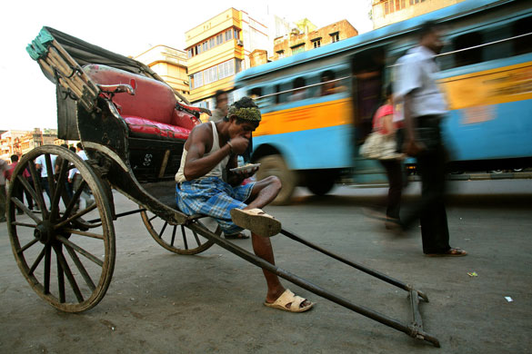14 April 2009: Kolkata, India: A rickshaw puller eats beside a busy road