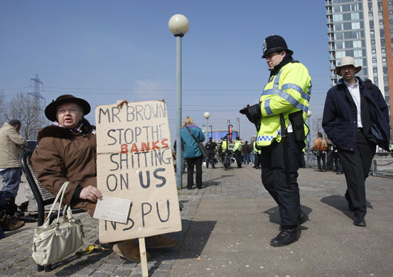 G20 protests day two: A policeman looks on as an elderly woman demonstrates at the ExCeL Centre.