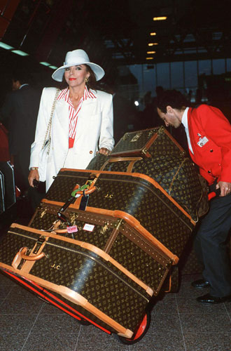 Joan Collins style icon: Joan Collins wearing a white suit and hat with Louis Vuitton luggage 