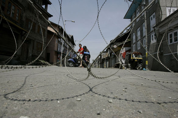29 April 2009: Srinagar, India: People ride a scooter near a barbwire road block