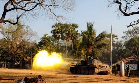 A Sri Lankan soldier stands near a tank as it ﬁres a shell at Puthukkudiyiruppu
