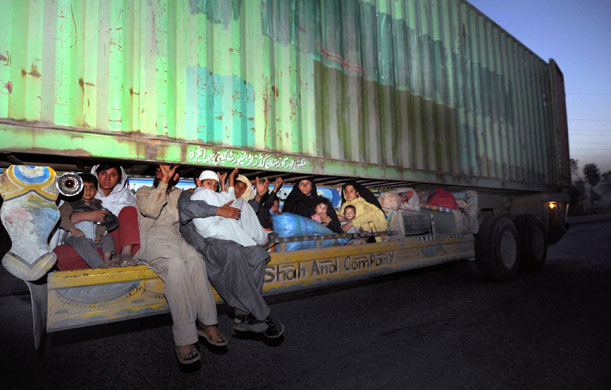 Pakistan Swat exodus: Displaced Pakistanis hitch a ride underneath a container truck