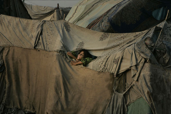 14 May 2009: Lahore, Pakistan: A girl looks out from her make-shift home