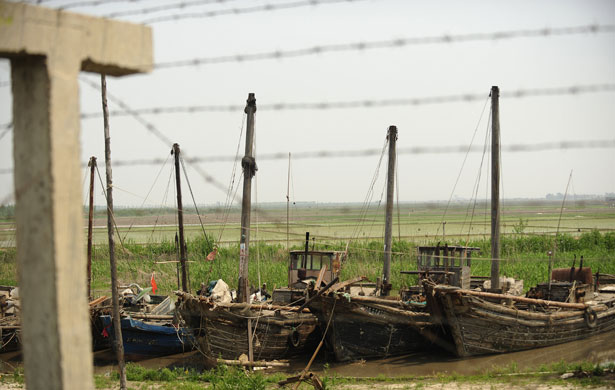 North Korea : Disused fishing boats rest behind a barbed wire fence 