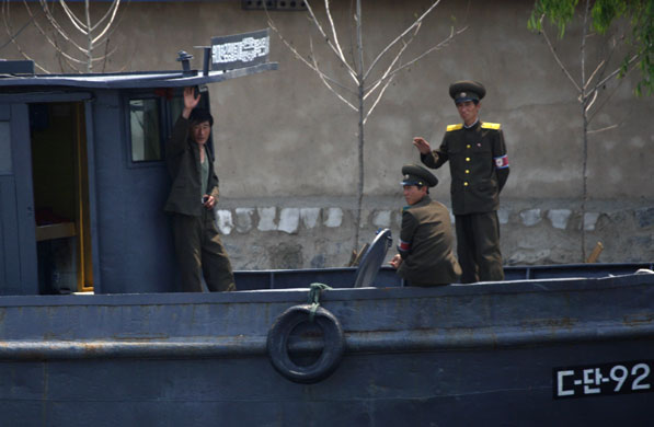 North Korea : North Koreans wave at a passing Chinese tour boat on the Yalu River