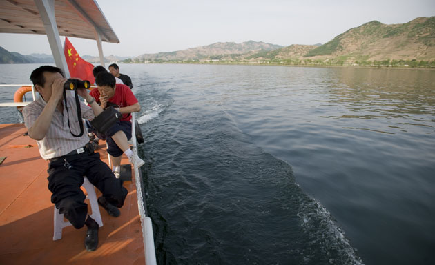 North Korea Border: Chinese tourists look at North Korea from a boat cruise along Yalu river