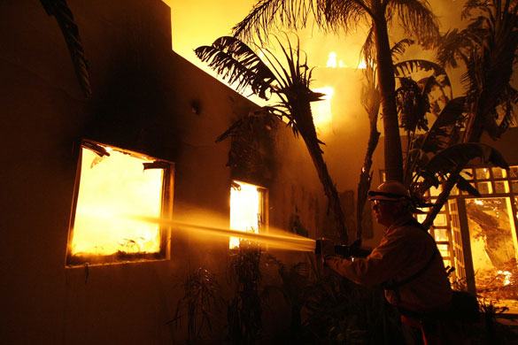 California Wildfires: A firefighter sprays water on a house burning