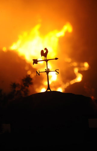 California Wildfires: Roof-top weather vane is silhouetted by oncoming flames