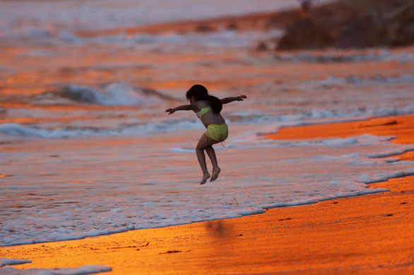 California Wildfires: A child plays in surf reddened by the reflection of heavy smoke overhead 