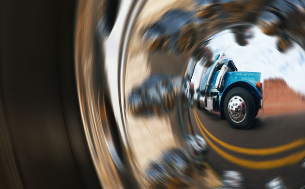 megatrucks: Semi-truck reflecting in hub cap of another truck on highway