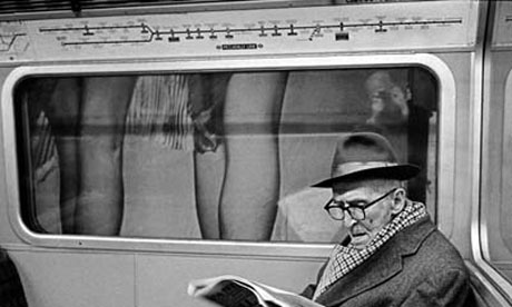 An older man reading a newspaper on a London underground tube train