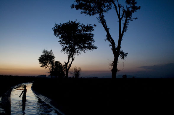 24 hours: A man bathes in a canal as the sun sets in Chota Lahore relief camp in Pakistan