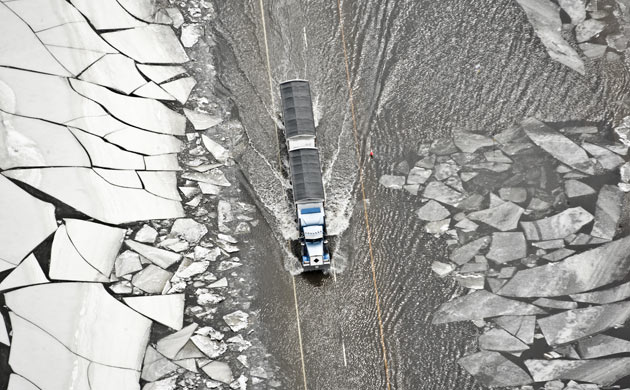 A semi-truck and trailer drives through floodwater and ice slabs